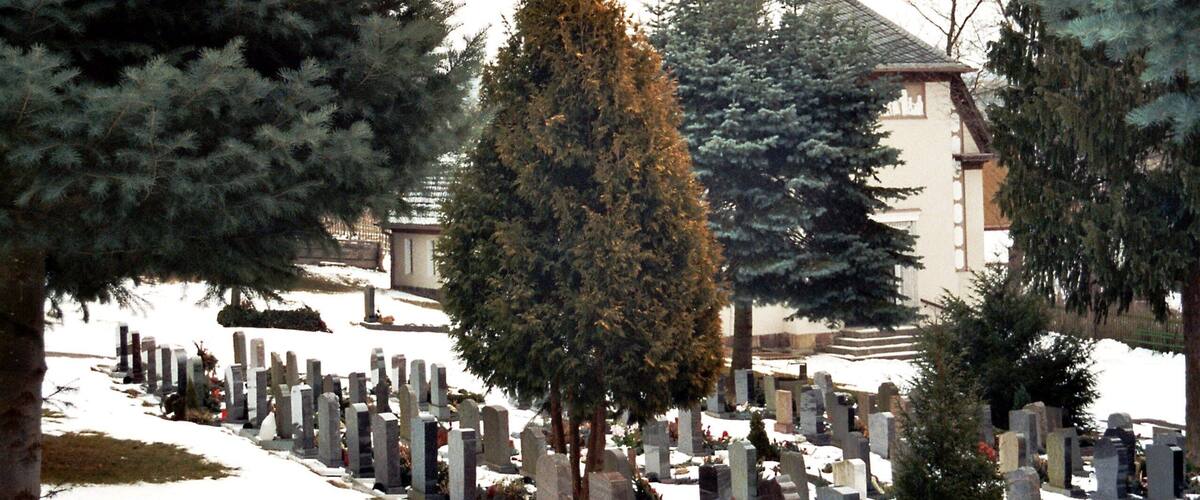 A cemetery with numerous headstones and a church with a dome in the background.
