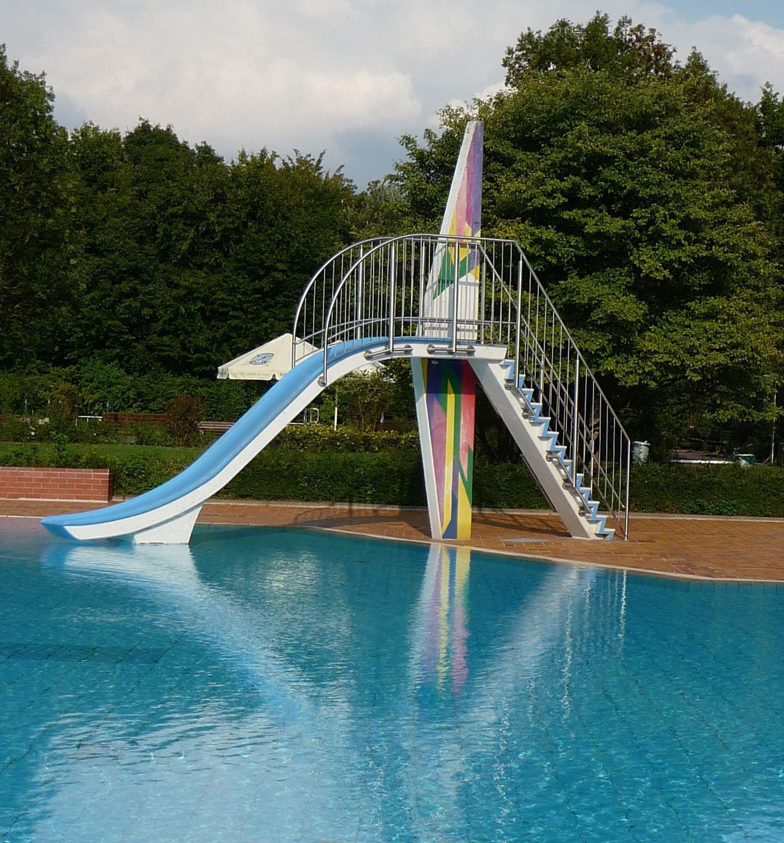 A swimming pool with a blue slide and a colorful staircase.