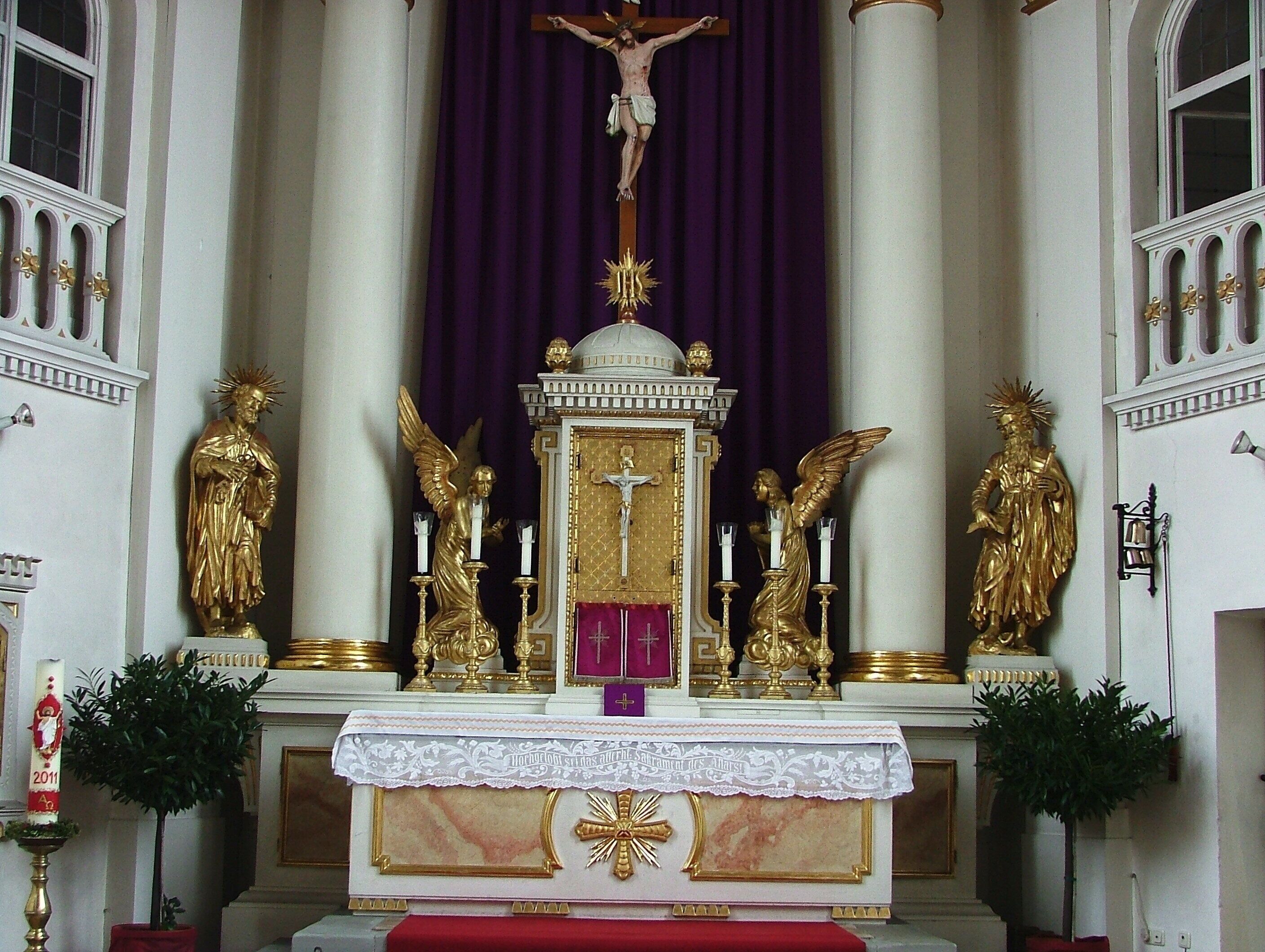 A church altar with a crucifix, golden statues, and a purple backdrop.