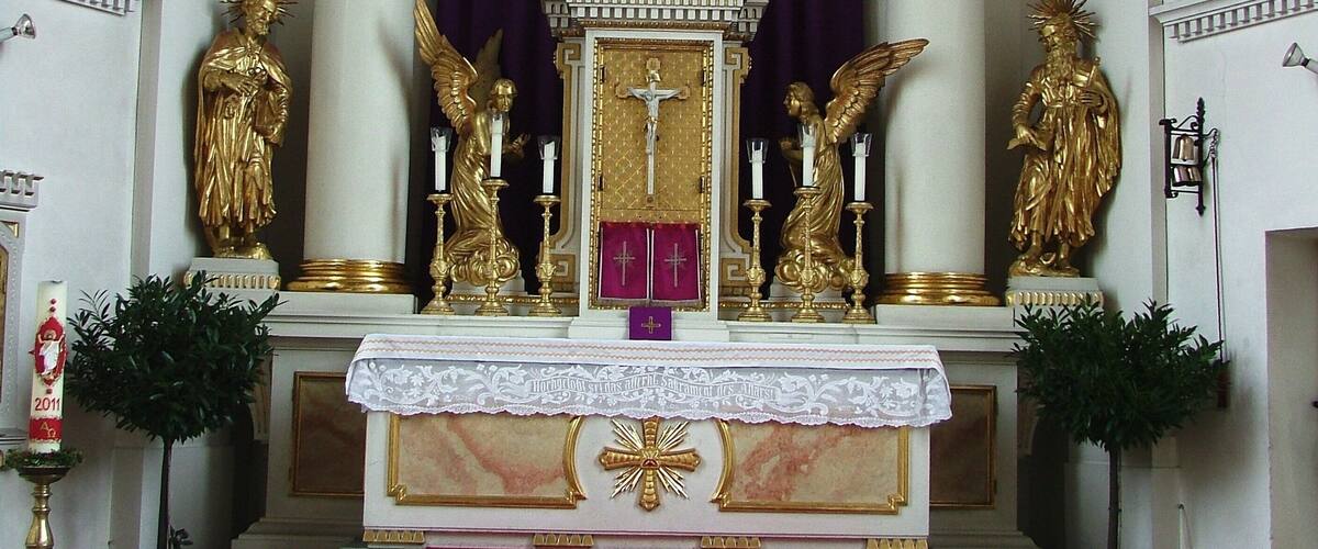 A church altar with a crucifix, golden statues, and a purple backdrop.