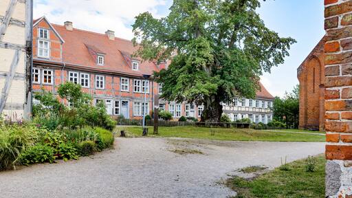 Ein Kiesweg führt zu einer Reihe traditioneller Backsteinhäuser mit roten Ziegeldächern und weißen Fensterrahmen.