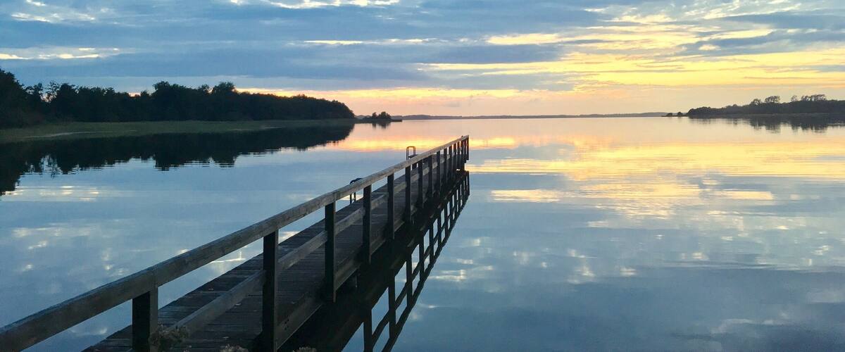 A wooden pier extending into calm waters with a sunset sky.