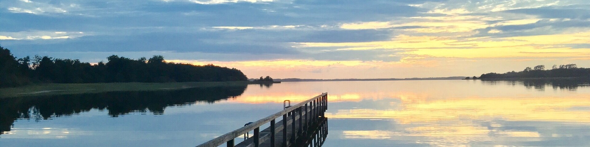 A wooden pier extending into calm waters with a sunset sky.