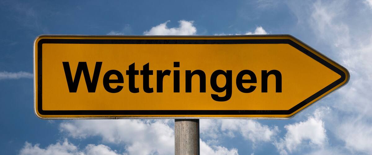 A directional sign with the word "Wettringen" against a blue sky with clouds.