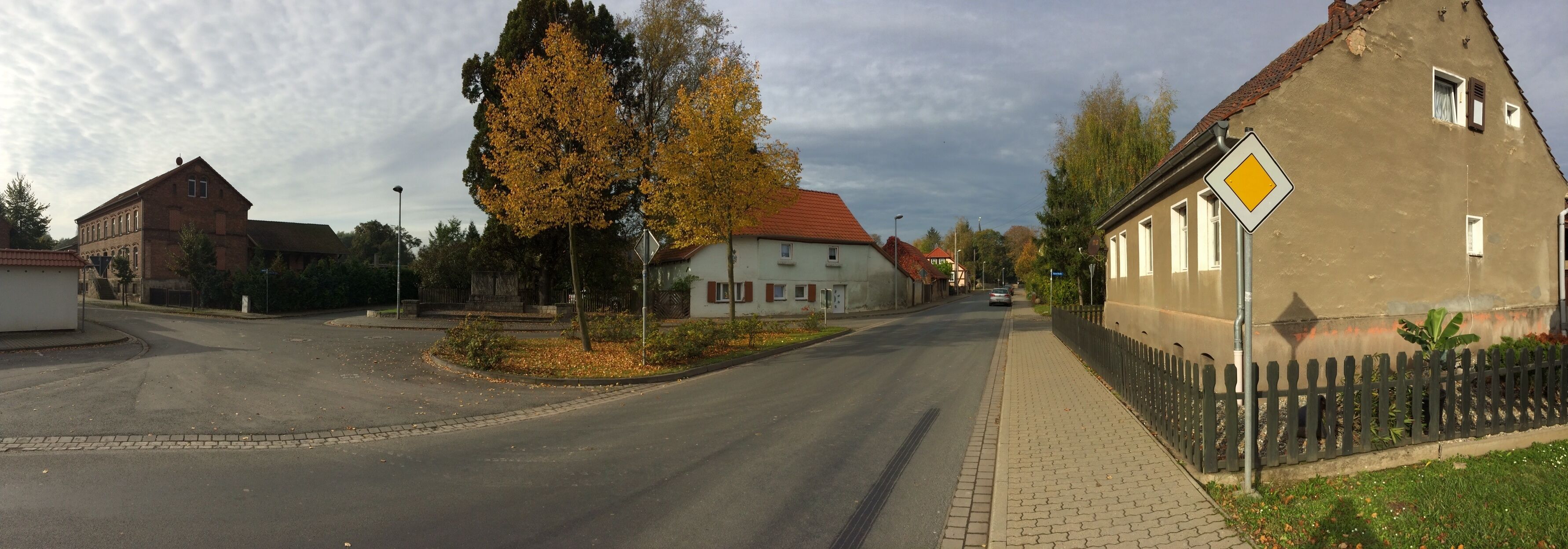 A quiet street with autumn trees, a roundabout, and traditional houses.