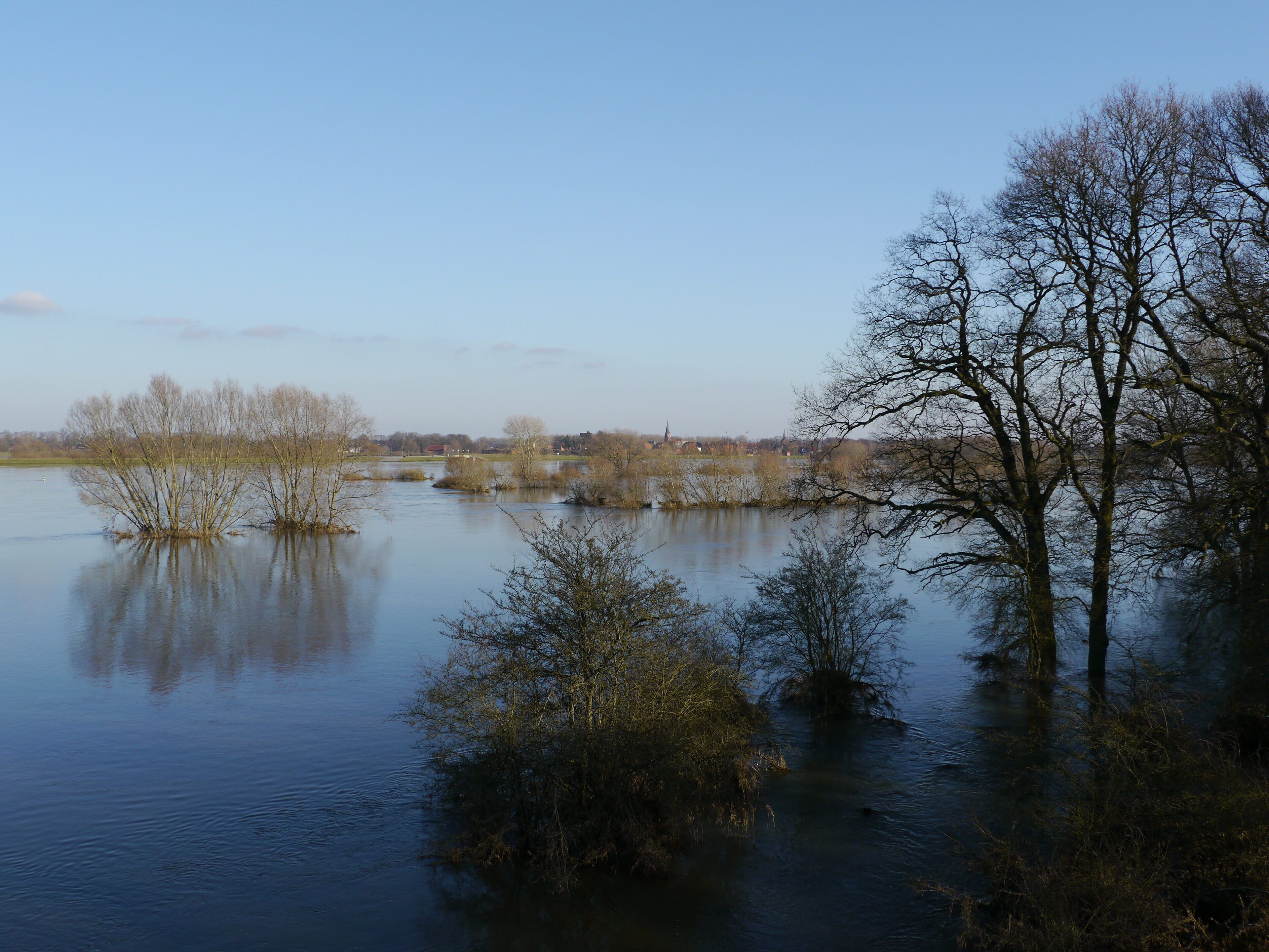 A calm river with trees and a distant bridge.