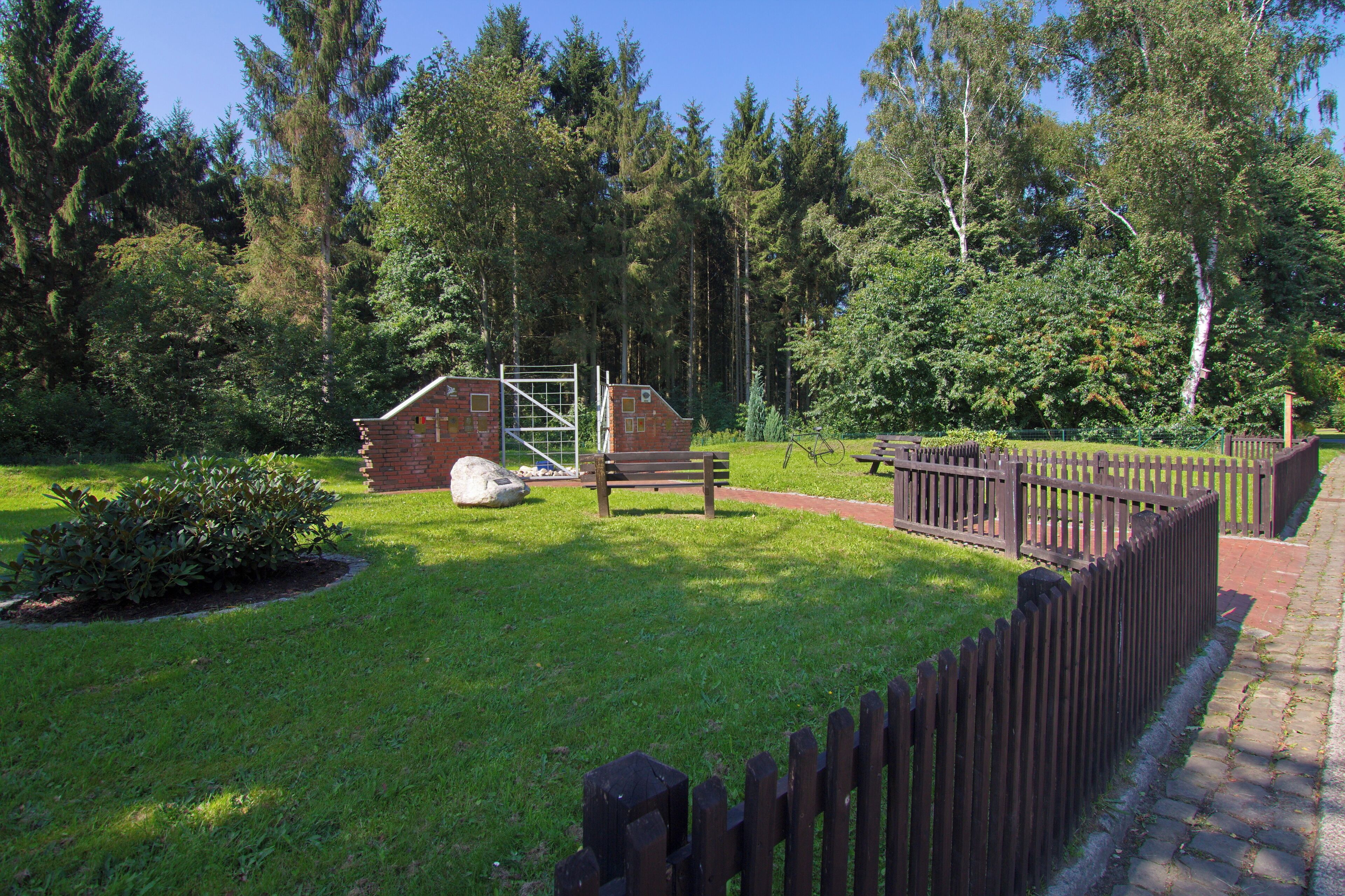 A park with a wooden bench, a brick structure, and a fenced area.