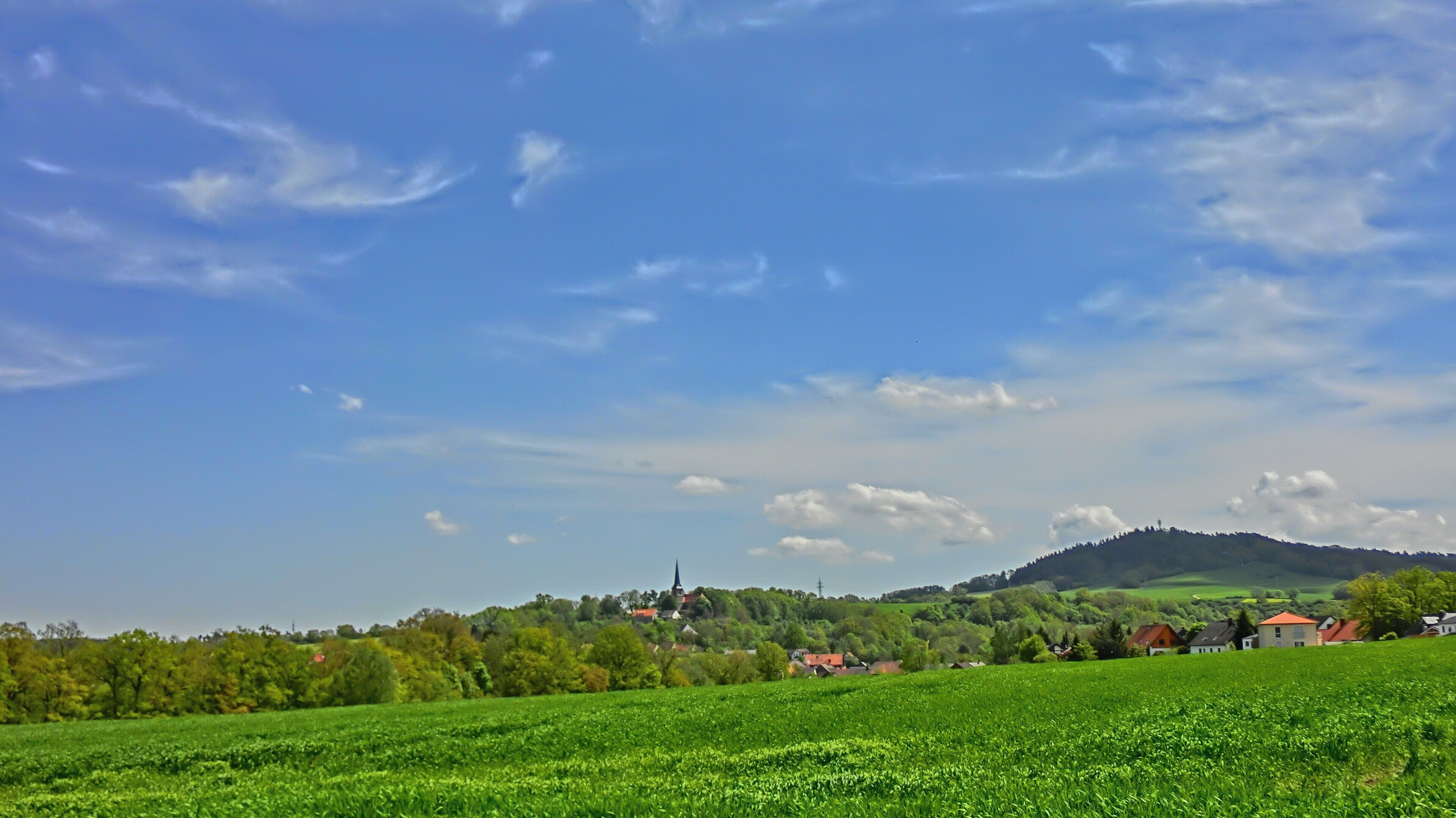 A green field, a village, and a hill with a church.