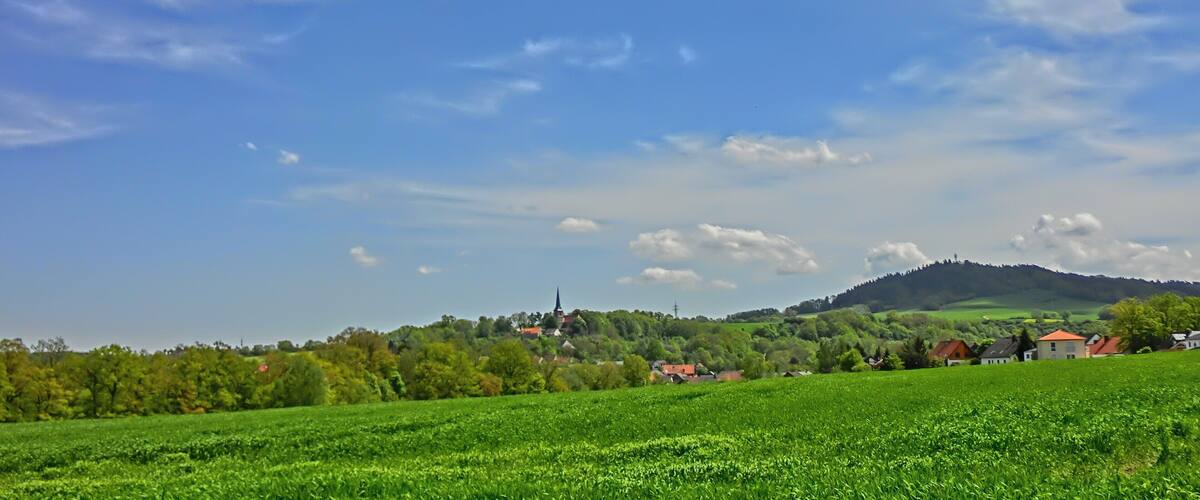 A green field, a village, and a hill with a church.