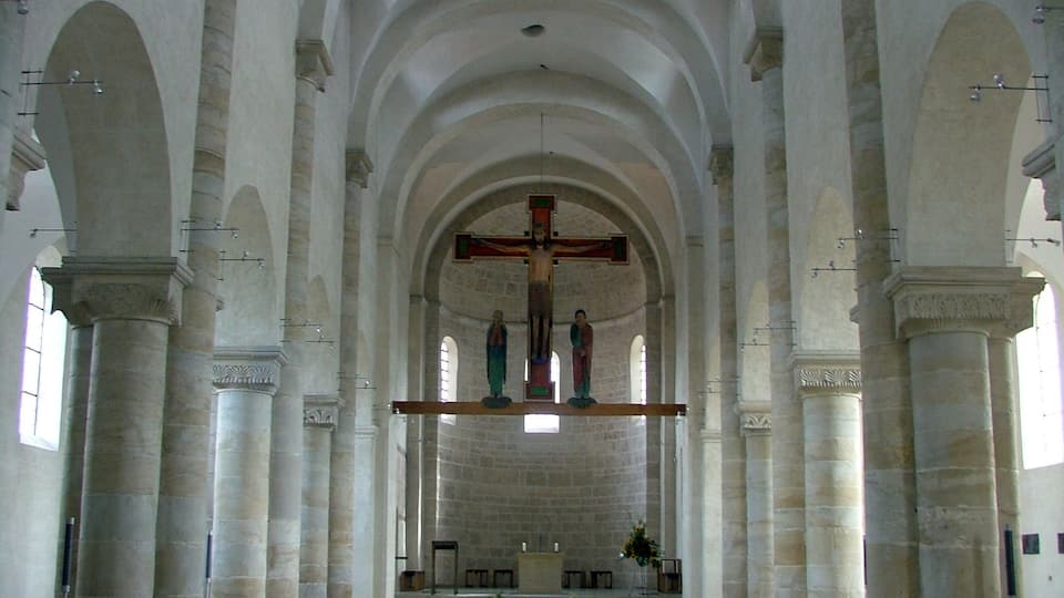 A church interior with high arched ceilings, a central cross, and rows of wooden pews.