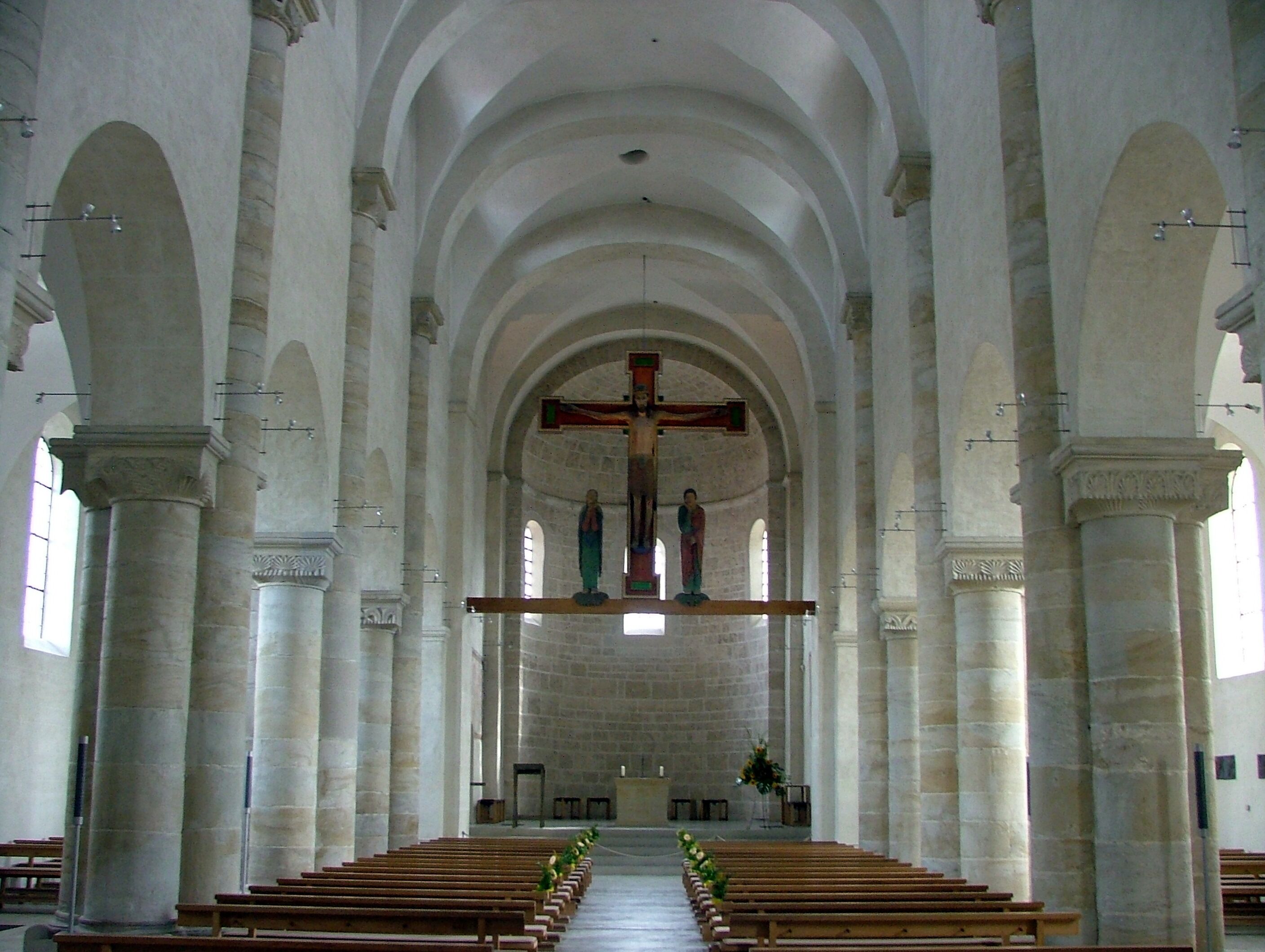A church interior with high arched ceilings, a central cross, and rows of wooden pews.