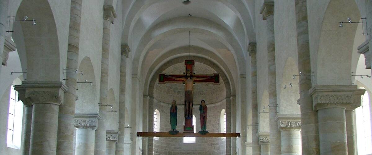 A church interior with high arched ceilings, a central cross, and rows of wooden pews.