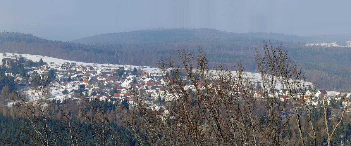A snow-covered town nestled in a valley with surrounding mountains and forests.