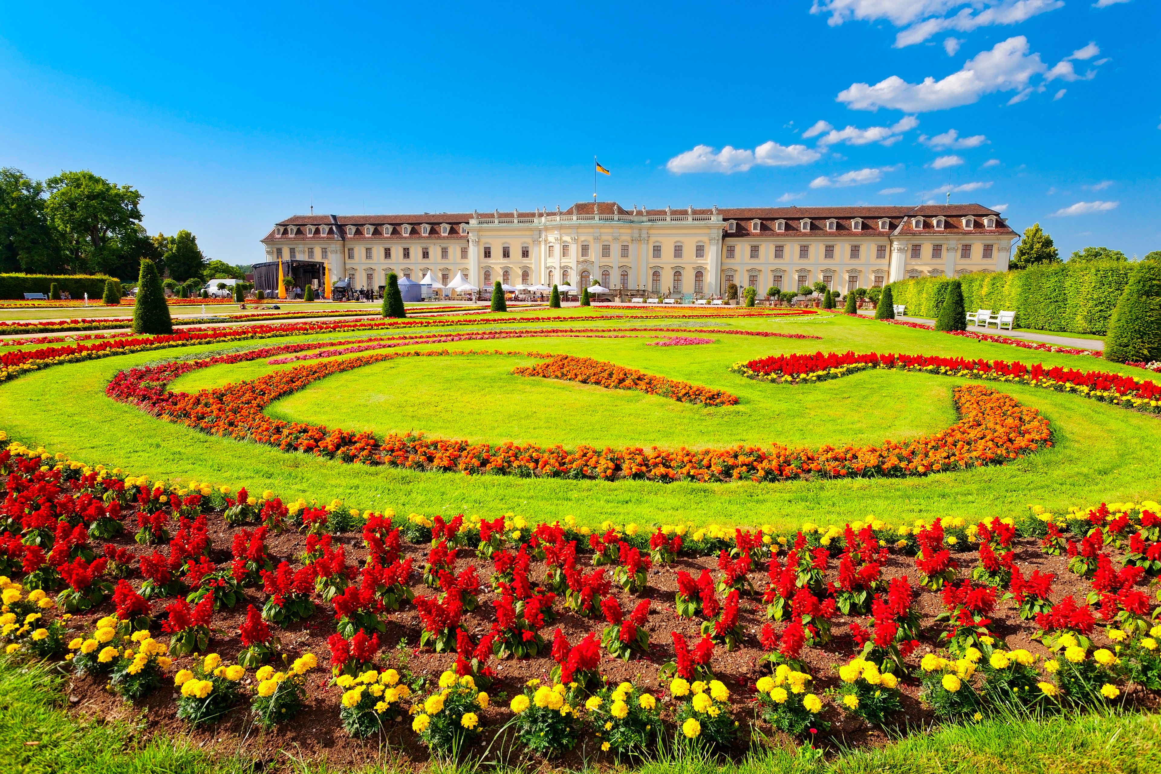 A grand palace with a symmetrical garden featuring vibrant flower beds and manicured lawns.