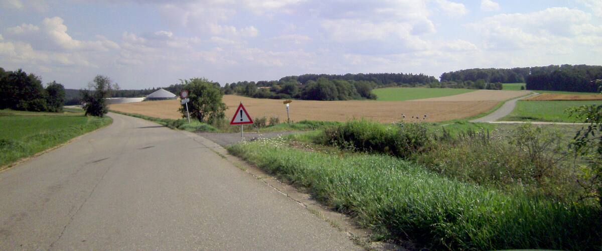 A rural road with a triangular warning sign, fields, and a partly cloudy sky.