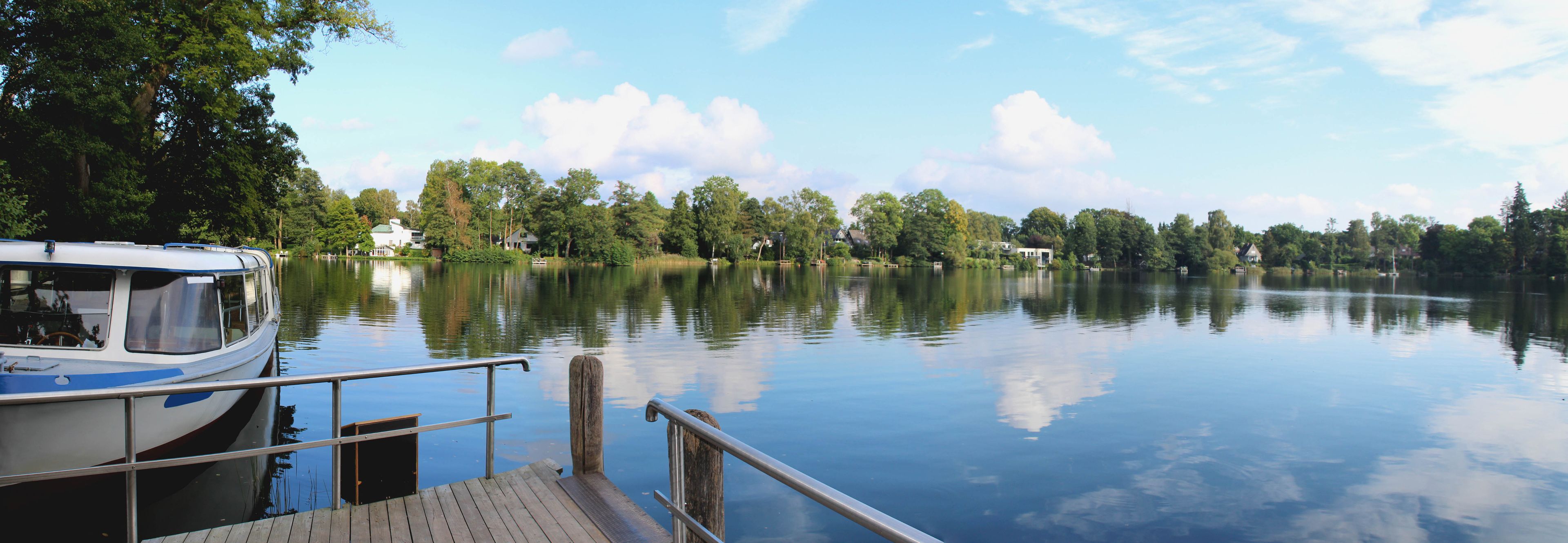 A calm lake with a dock, surrounded by trees and houses.