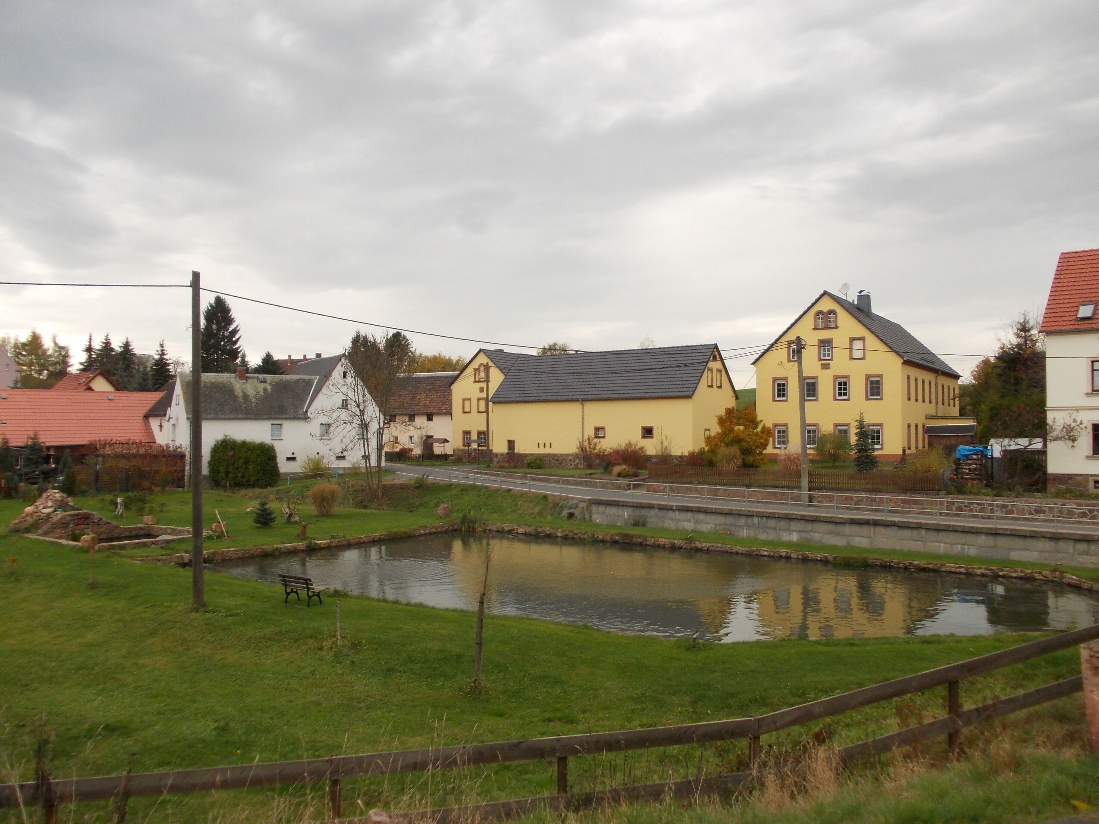 A small pond surrounded by houses with a cloudy sky.