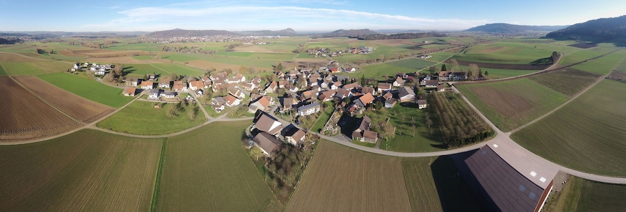An aerial view of a rural village with houses, fields, and a mountain in the background.