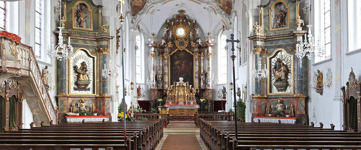 An ornate church interior with wooden pews, a central altar, and elaborate wall decorations.
