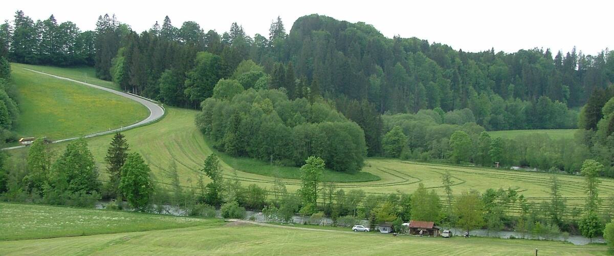 A rural landscape with rolling hills, a winding road, and a cluster of houses near the road.