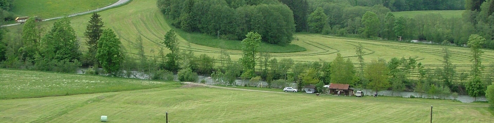 A rural landscape with rolling hills, a winding road, and a cluster of houses near the road.