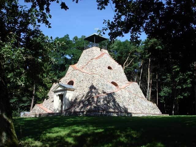 A stone structure with a small building at its base, surrounded by trees.