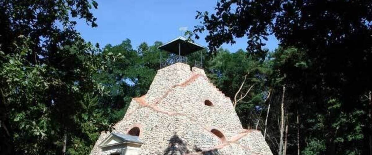 A stone structure with a small building at its base, surrounded by trees.