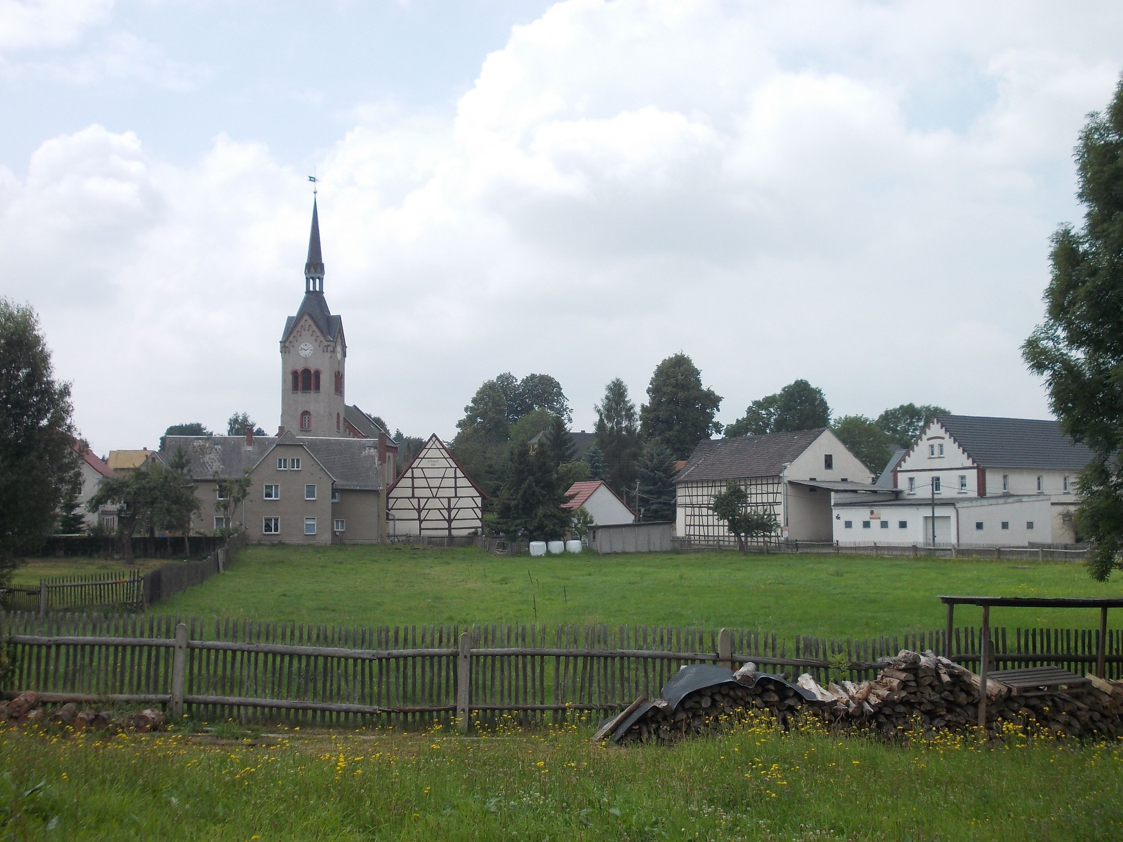 A church with a tall steeple, a traditional half-timbered house, and a white building with a gabled roof.