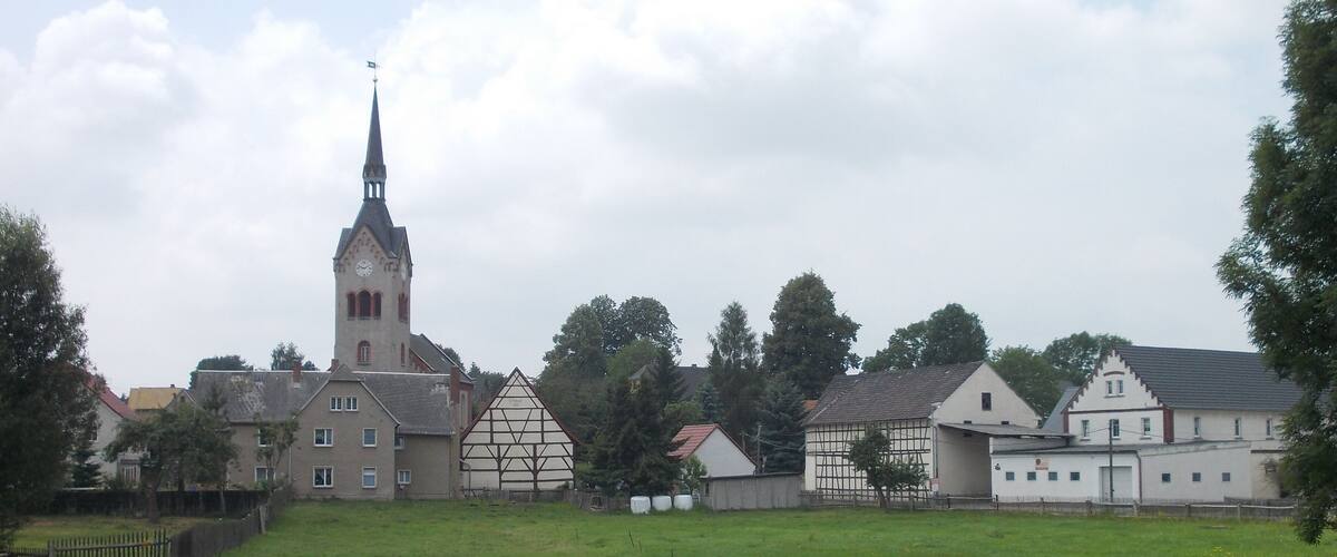 A church with a tall steeple, a traditional half-timbered house, and a white building with a gabled roof.