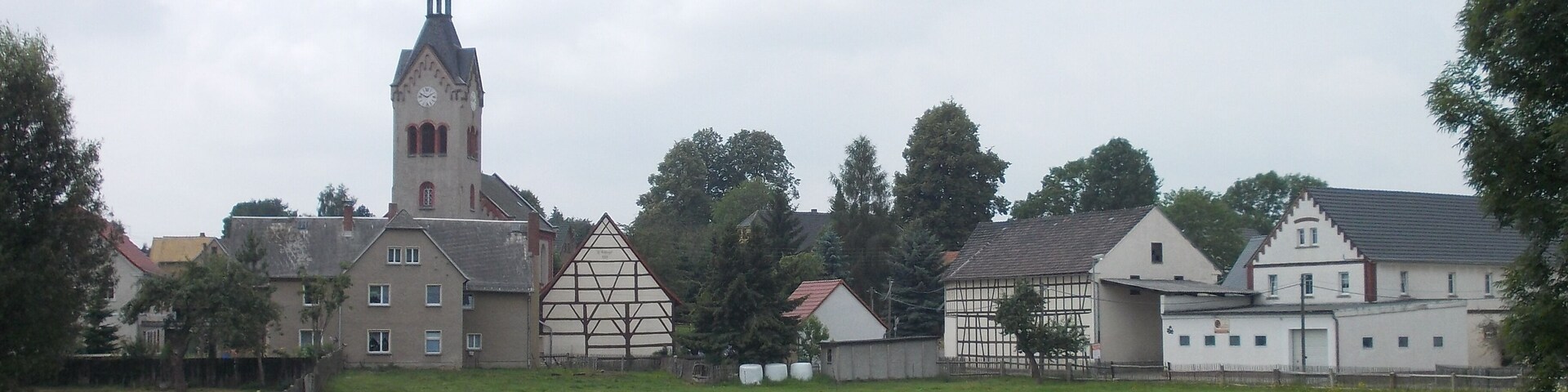 A church with a tall steeple, a traditional half-timbered house, and a white building with a gabled roof.