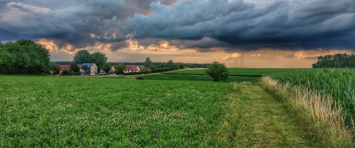 A rural landscape with fields, a farmhouse, and a cloudy sky.