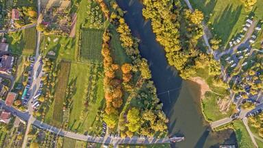 An aerial view of a riverside area with fields, trees, and RVs parked along the road.