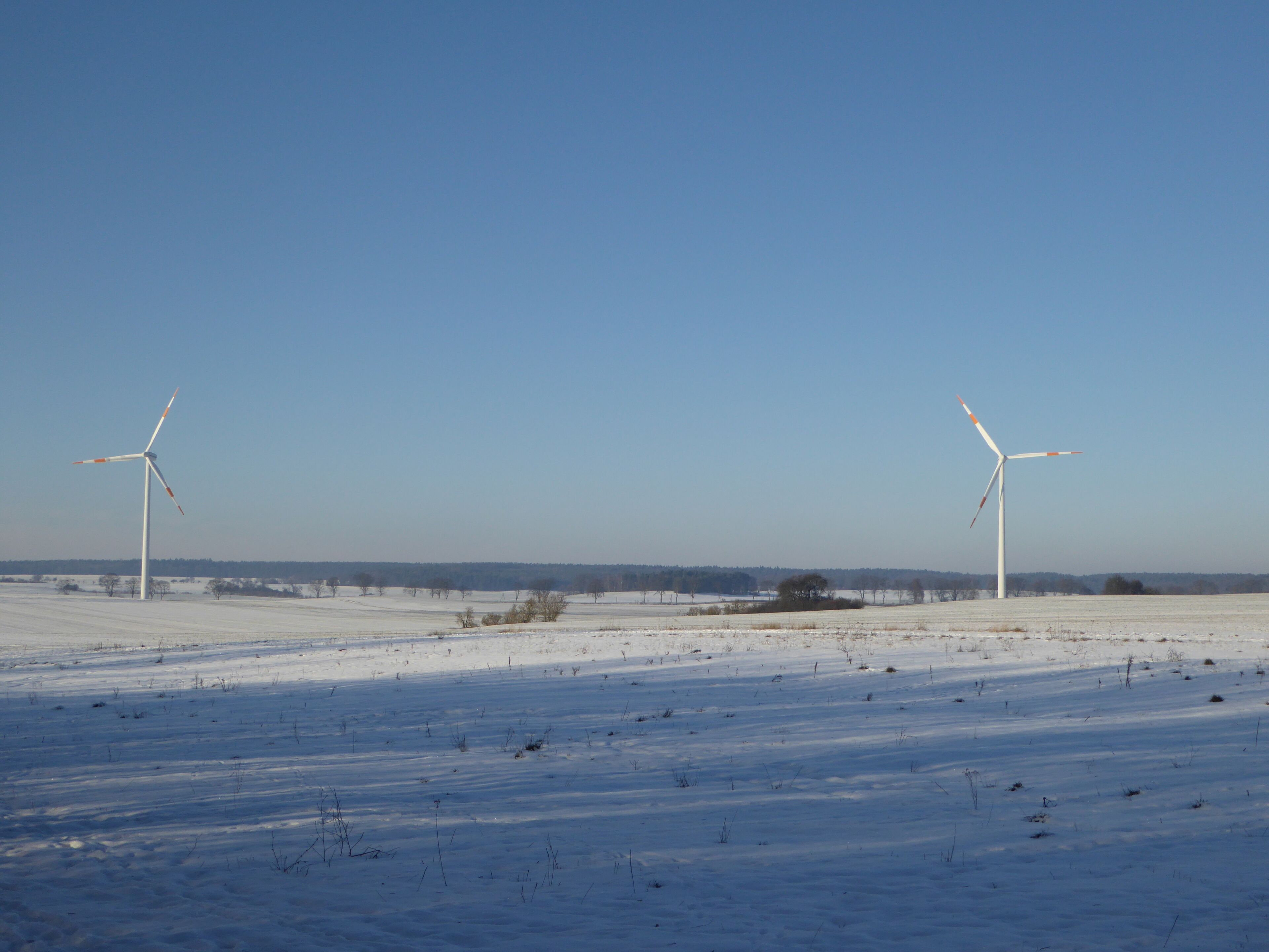 A snowy landscape with two wind turbines.