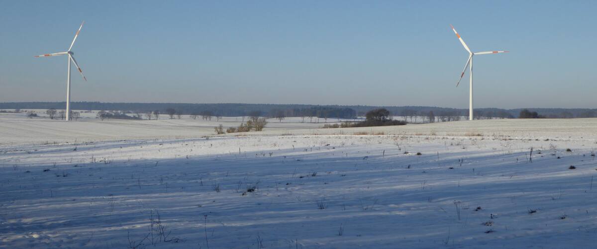 A snowy landscape with two wind turbines.