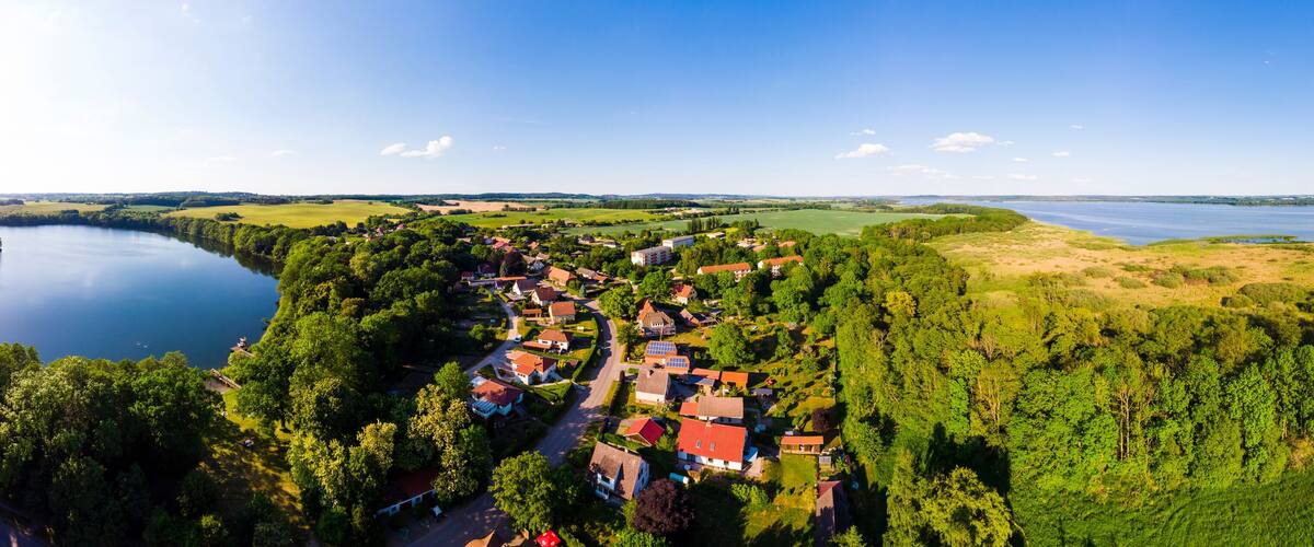 A lakeside village with red-roofed houses, surrounded by dense forests and fields.
