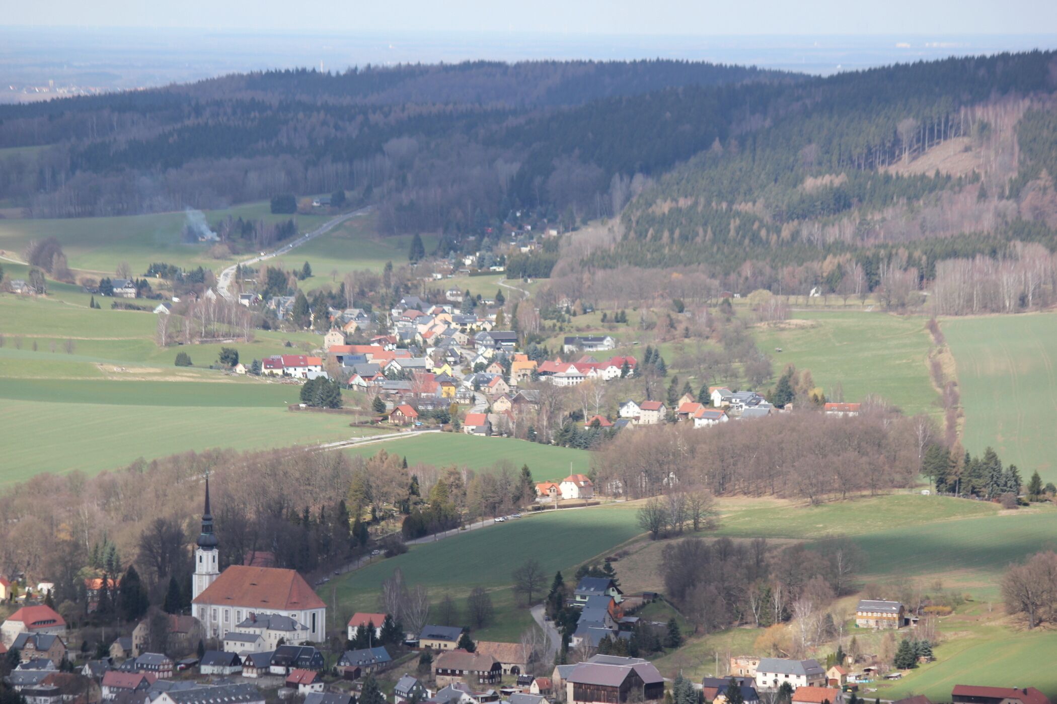 A rural town nestled in a valley with a prominent church and rolling hills in the background.