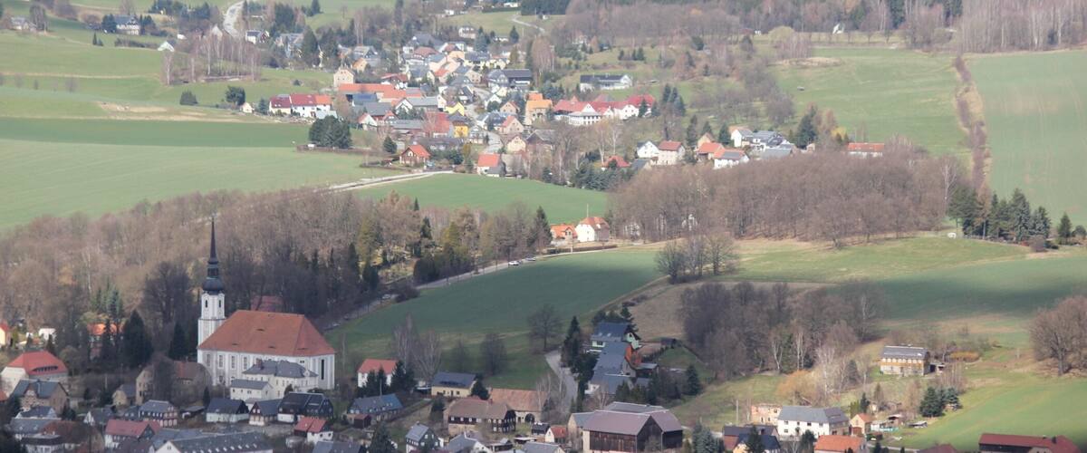 A rural town nestled in a valley with a prominent church and rolling hills in the background.