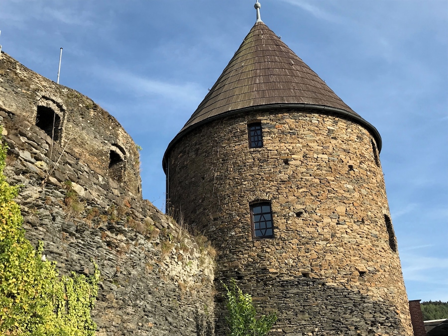 Uma torre de pedra com telhado cônico e uma torre menor adjacente com aberturas em arco.