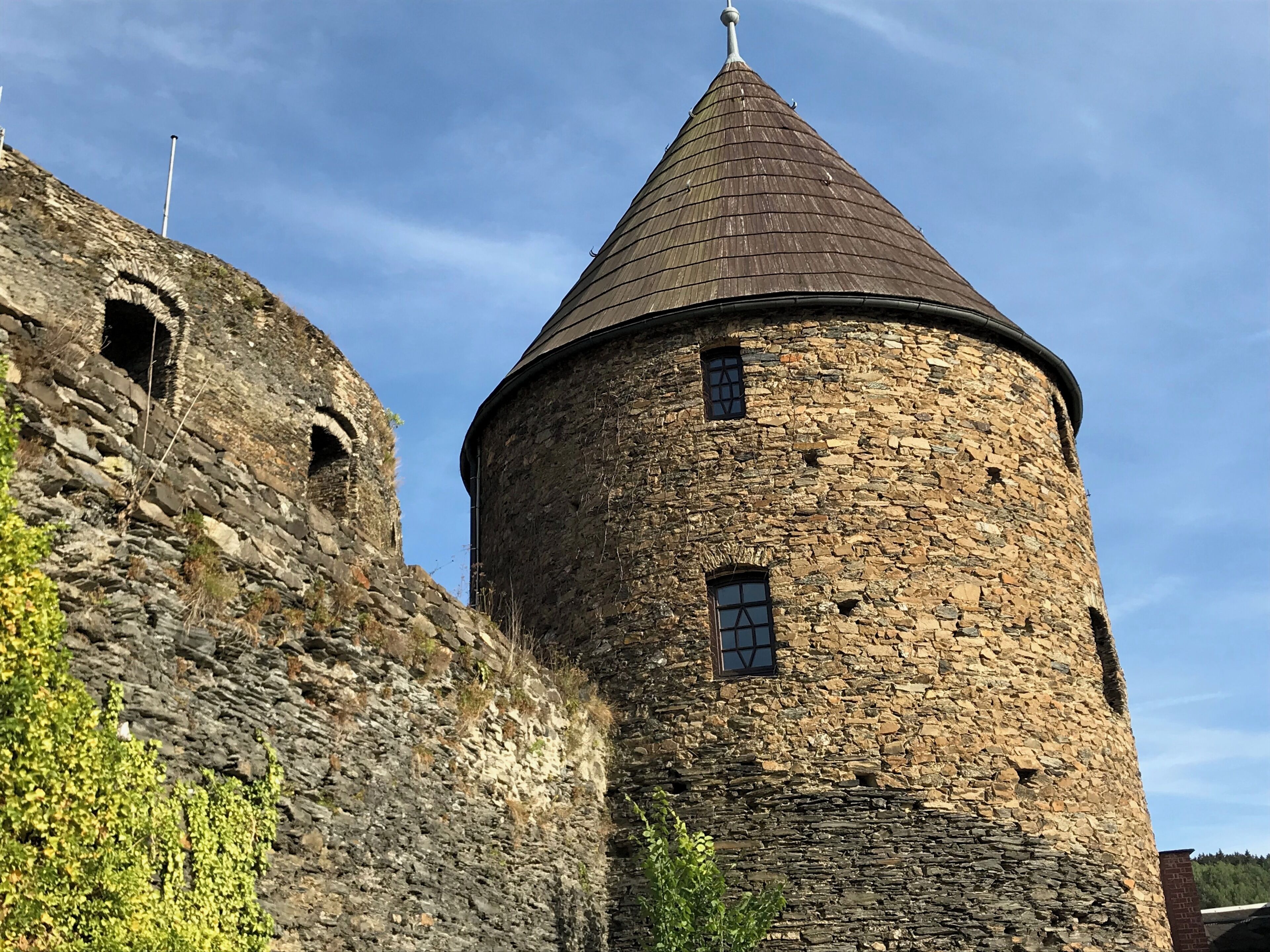 A stone tower with a conical roof and a smaller adjacent tower with arched openings.