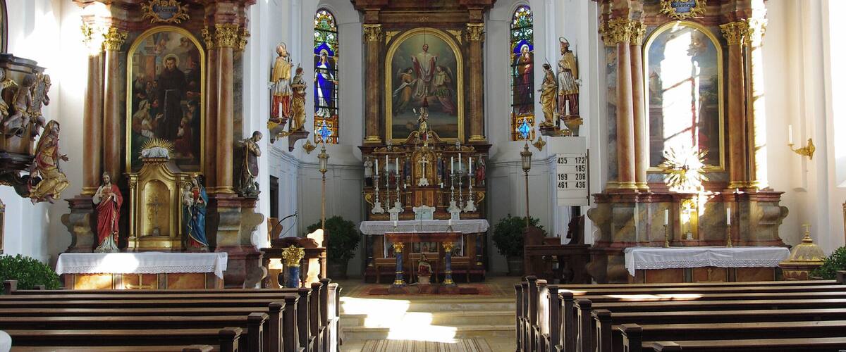 An ornate church interior with a central altar, stained glass windows, and rows of pews.