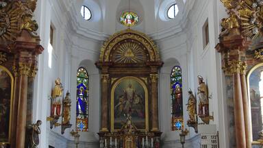Een sierlijk kerkinterieur met een hoog plafond, een kroonluchter, glas-in-loodramen en religieuze beelden.