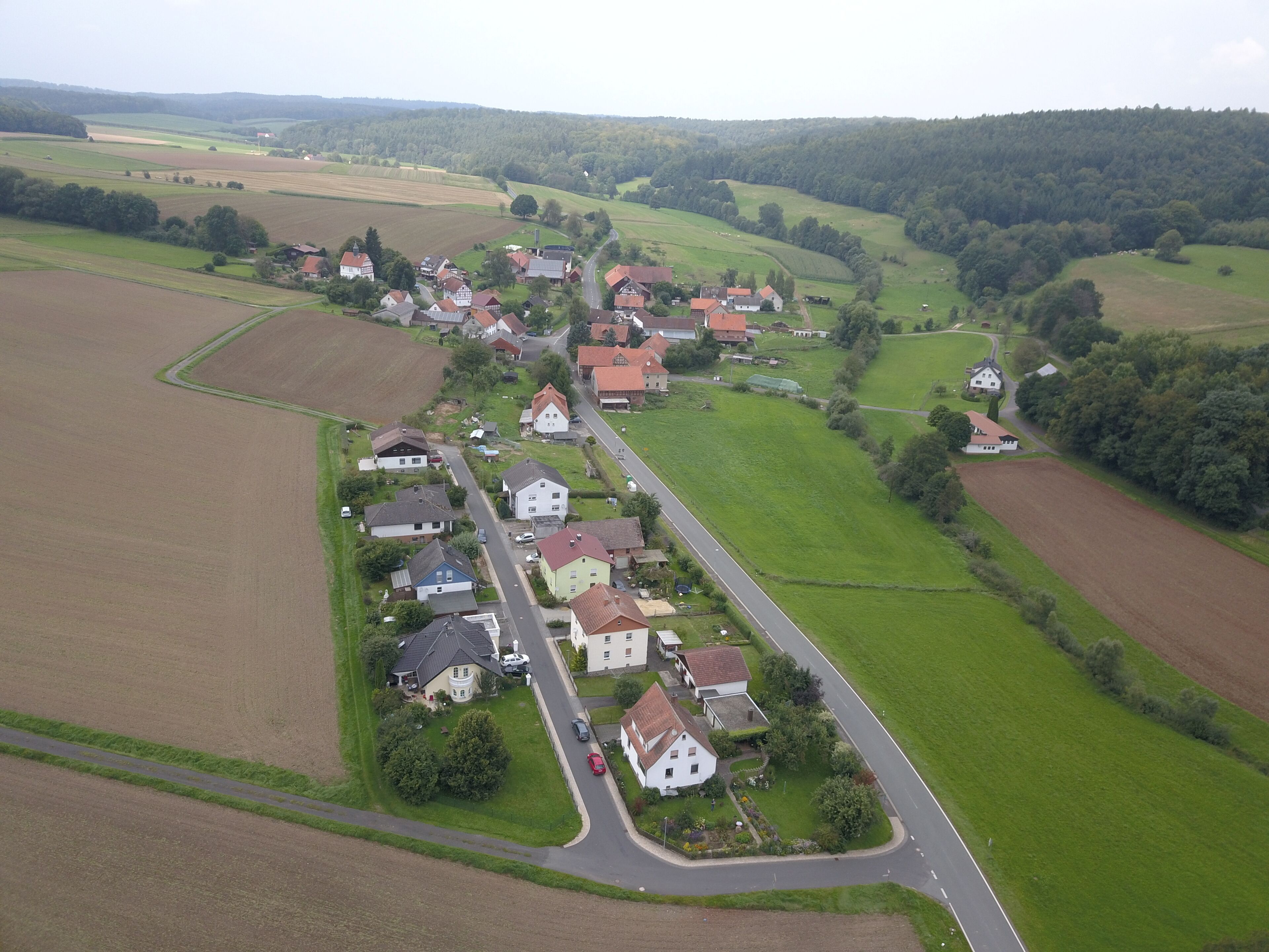 An aerial view of a rural village with houses, roads, and surrounding fields.