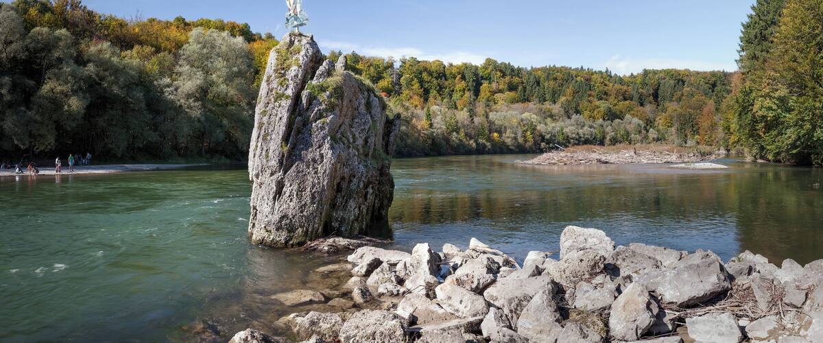 A rocky outcrop with a statue in a river surrounded by autumn foliage.