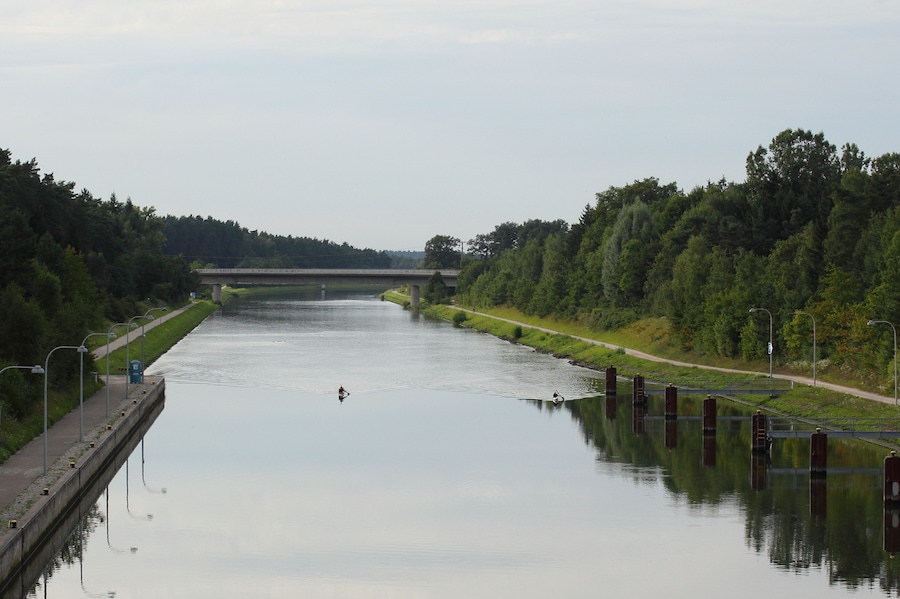 A calm river with a bridge in the distance, surrounded by dense greenery.