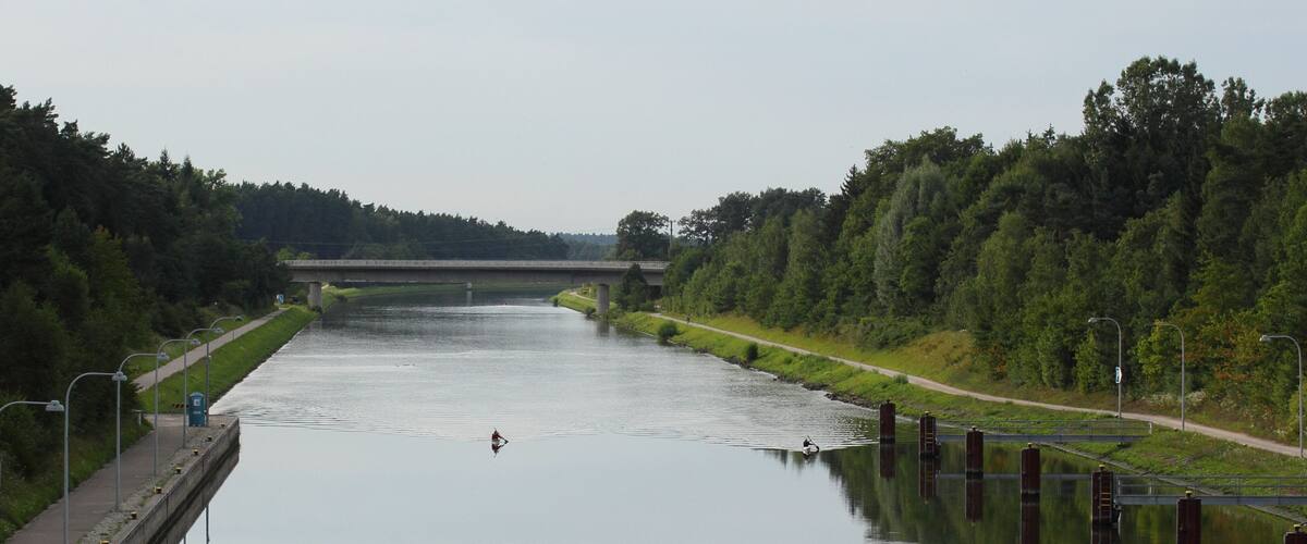 A calm river with a bridge in the distance, surrounded by dense greenery.
