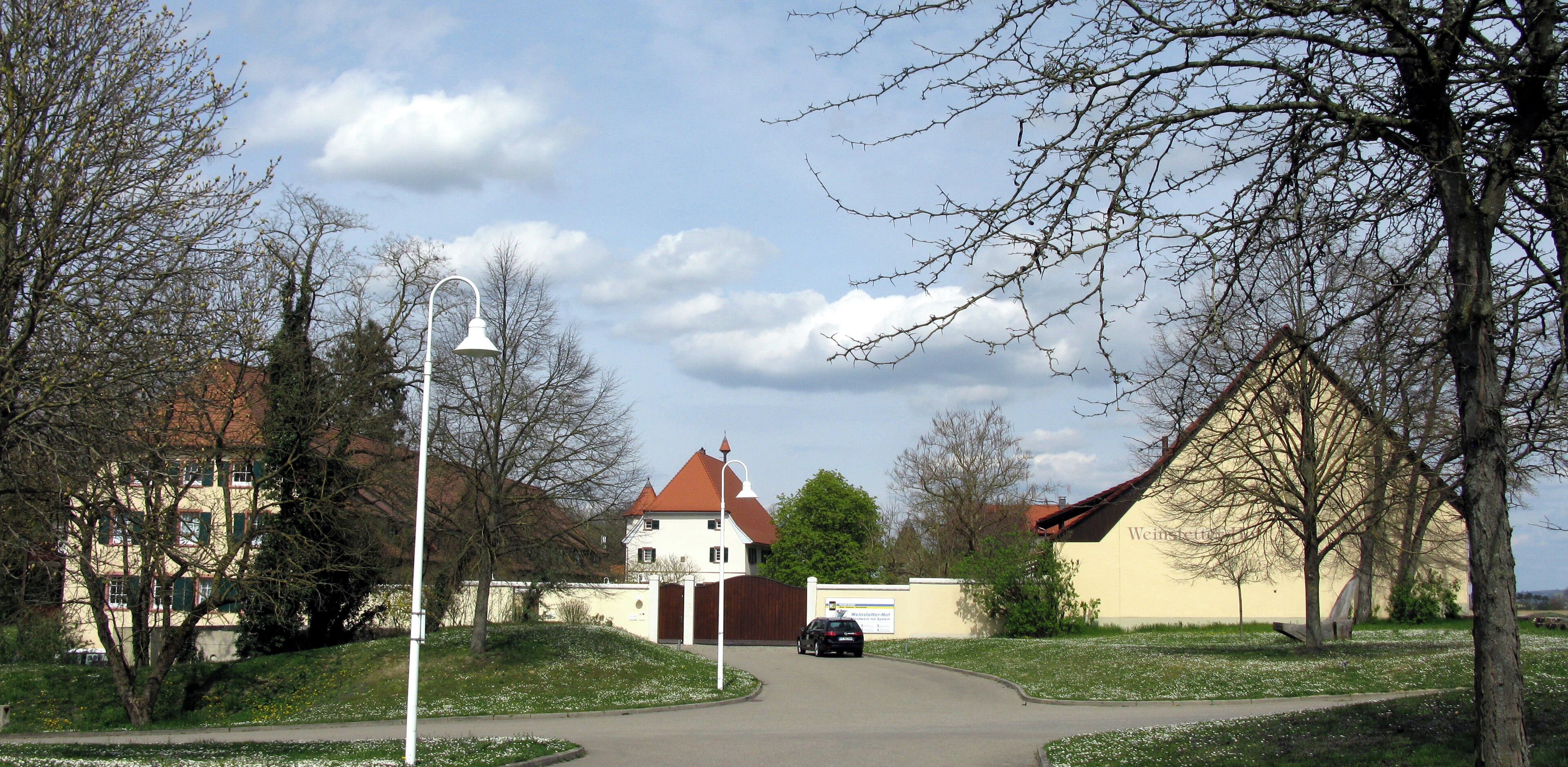 A tree-lined street with a white building with a red roof, a street lamp, and a car parked on the side.