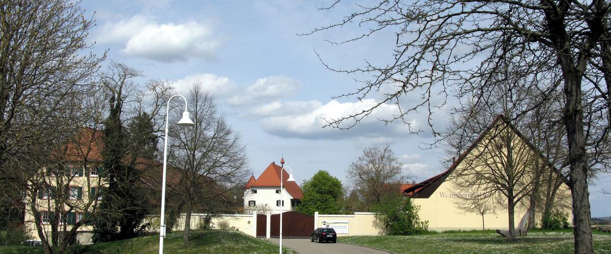 A tree-lined street with a white building with a red roof, a street lamp, and a car parked on the side.