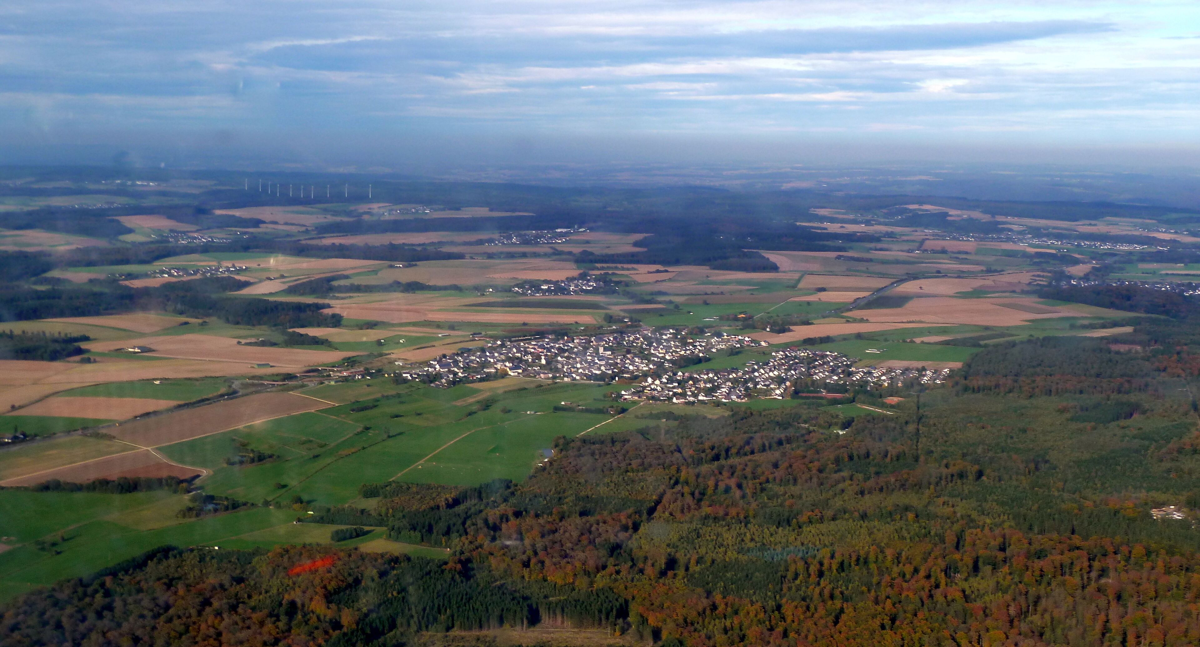 A rural landscape with a village, fields, and wind turbines.
