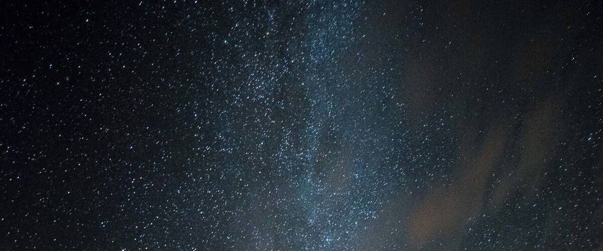 A starry night sky over a body of water with a distant building.