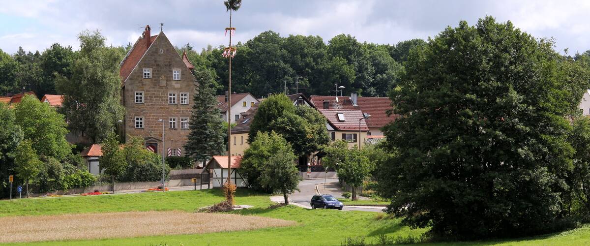 A green field, a large tree, and a building with a red roof.